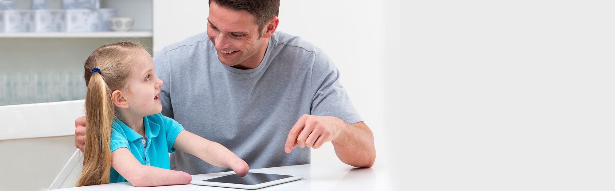 Man sits with daughter who has no hands at a table looking at a tablet